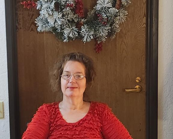 Photo of Christine sitting front of a door with a wreath.