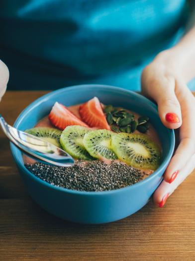 woman eating a healthy meal of fruits and yogurt in blue bowl