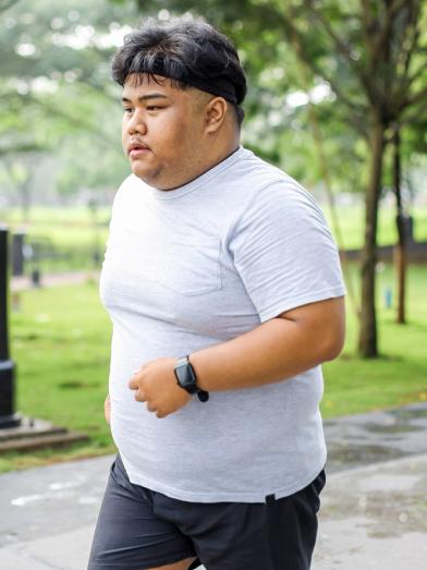 An overweight man outside jogging to reduce his weight and treat obesity 