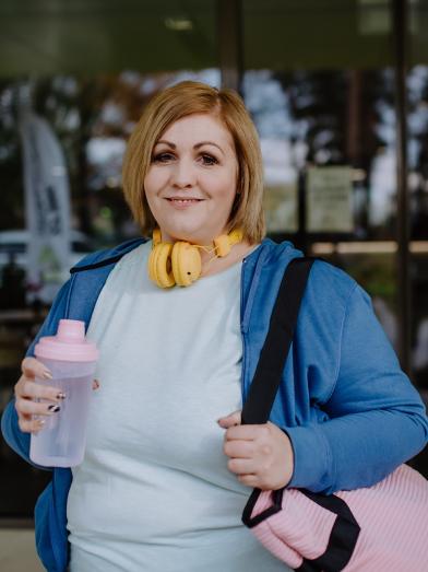 An overweight woman smiling while heading to the gym with water to overcome obesity and stress