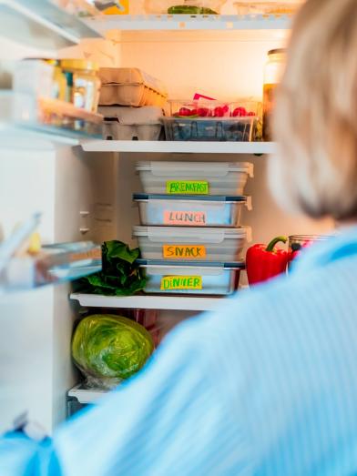 A person standing in front of a fridge with labeled containers for meal prep